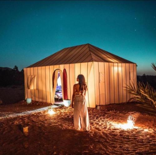 uma mulher em pé em frente a uma grande tenda em Merzouga luxurious Camp em Merzouga
