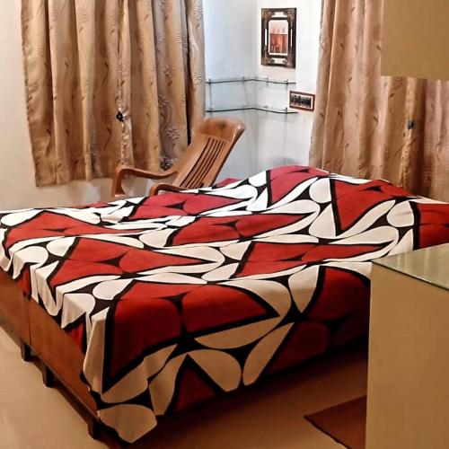 un letto con una coperta rossa e bianca e una sedia di Parthasarathy Home stay a Trivandrum