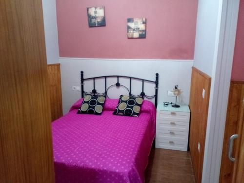 a bedroom with a pink bed with black pillows at Apartamento araceli in Chipiona