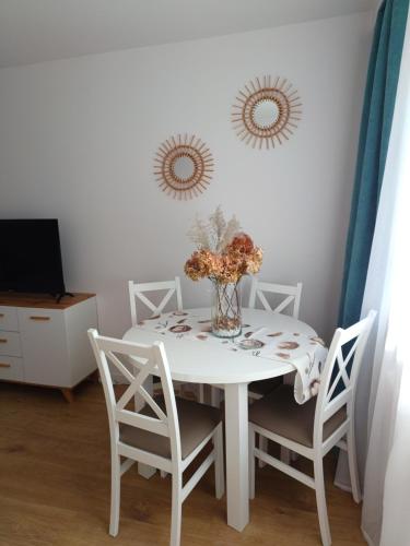 uma mesa de jantar branca com cadeiras e um vaso com flores em Apartament Turkusowy em Gdansk