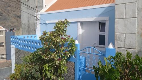 a blue fence and a house with a tree at Casa Mrichica in Mão para Trás