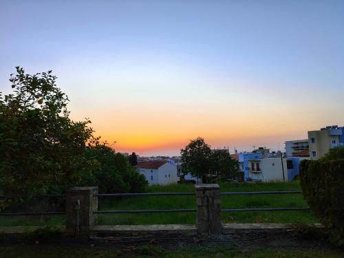 a sunset over a field with a fence and buildings at Cozy Nest in Karlovasi