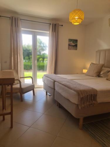 een slaapkamer met een bed, een stoel en een raam bij Cabanas Garden By HnM in Cabanas de Tavira