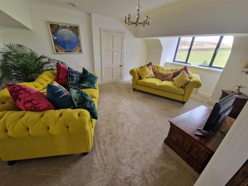 a living room with two yellow couches and a tv at Oakenclough Hall in Macclesfield
