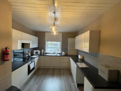 a large kitchen with white cabinets and black counter tops at Gateway to the Loch in Balloch