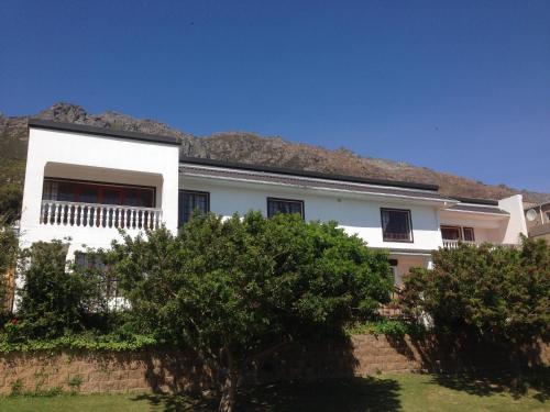 a white house with a blue roof and trees at Helderberg Guesthouse in Gordonʼs Bay