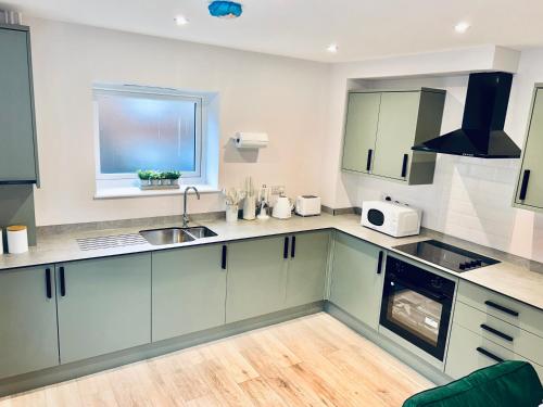 cocina con armarios verdes, fregadero y ventana en Port of Dover Apartments en Kent