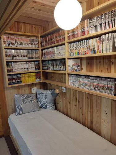 a room with a bed in a library with wooden shelves at The Gold Beach House in Daisen
