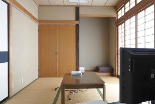 a room with a tv and a table and a room with a door at 布施温泉ステイ　ウエスト in Saku