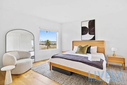 a bedroom with a bed and a chair and a mirror at Beach Street Luxury 3 Bed with Beach & Bay Views in Melbourne