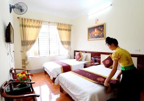 una mujer haciendo una cama en una habitación de hotel en Agri Hotel Điện Biên Phủ - by Bay Luxury, en Diện Biên Phủ