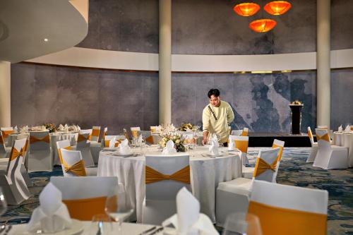 a man standing in a dining room with tables at Wyndham Hoi An Royal Beachfront Resort & Villas in Hoi An