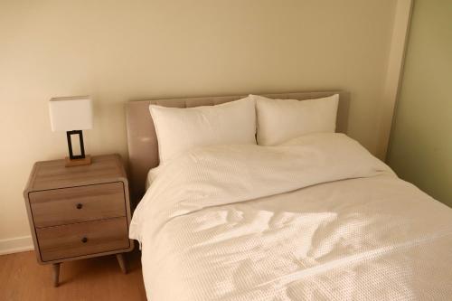 a bed with white sheets and a nightstand with a lamp at Downtown Dream in Toronto