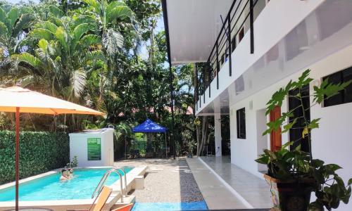 an outdoor swimming pool with an umbrella and a house at Casajungla Hostel in Jacó