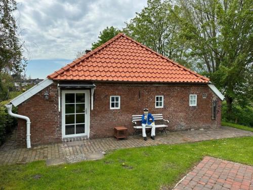 eine Person, die auf einer Bank vor einem Backsteingebäude sitzt in der Unterkunft Landhaus up Diek in Wittmund