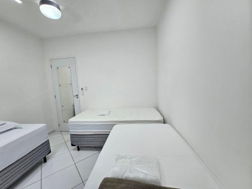 um quarto branco com 2 camas e um espelho em Quarto Privativo em Condominio no Rio de Janeiro