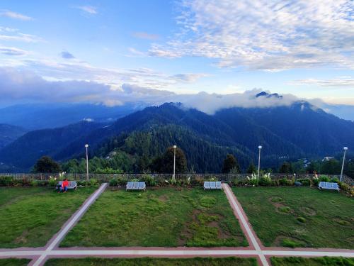 two benches in a field with mountains in the background at Hawk Eye Resort in Shimla