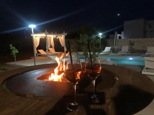 two glasses of wine sitting on a table next to a fire at B&B Casa Karina Pool&Rooms in Specchia