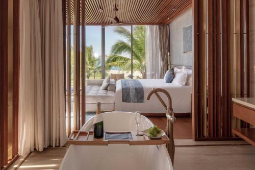 a bathroom with a tub and a bedroom with a bed at Wyndham Hoi An Royal Beachfront Resort & Villas in Hoi An
