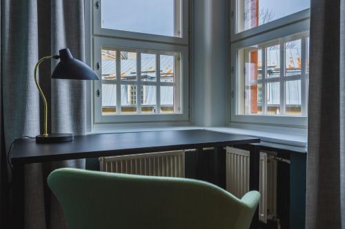 einen Schreibtisch mit einer Lampe und einem Stuhl vor zwei Fenstern in der Unterkunft Ineon Hotel in Turku