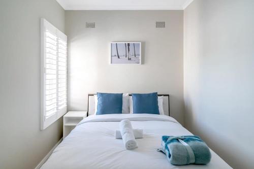 ein weißes Schlafzimmer mit einem Bett mit blauen Kissen in der Unterkunft Hall St - Hideaway in the Heart of Bondi Beach in Sydney