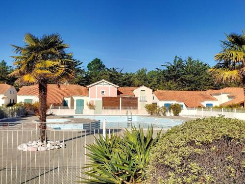 une clôture avec un palmier devant une maison dans l'établissement Maison avec piscine chauffée, à 500m de la plage et proche forêt - Terrasse, vélos inclus - FR-1-652-3, à Saint-Hilaire-de-Riez