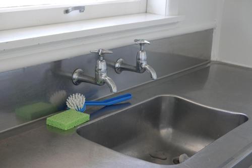 a kitchen sink with two faucets and a green sponge at Ascot Lodge Motel in Hamilton