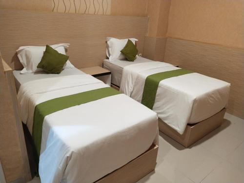 two beds in a small room with white and green sheets at Hotel Kembang Joyo in Palu