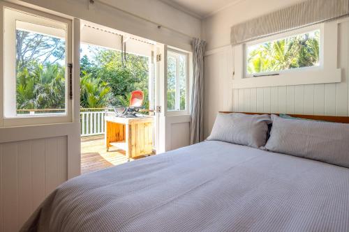 1 dormitorio con cama, ventanas y escritorio en Nikau Cottage - Palm Beach Holiday Home, en Palm Beach
