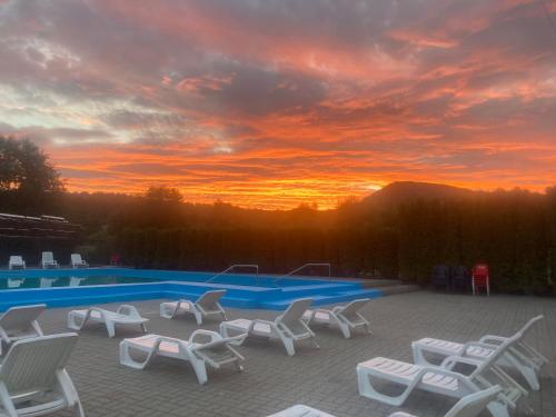 a group of chairs and a swimming pool at sunset at Pensiunea Hyperion Cormaia in Sîngeorz-Băi