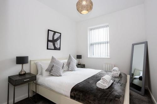 a bedroom with a bed with white sheets and a mirror at Contemporary Bolton Apartment in Central Location in Bolton