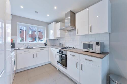 a white kitchen with white cabinets and a microwave at Spacious 3 Bedroom House with Garden in Birmingham in Birmingham