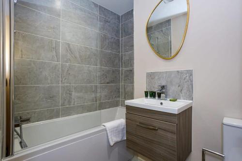 ein Badezimmer mit einem Waschbecken, einer Badewanne und einem Spiegel in der Unterkunft Stylish and Bright 2 Bedroom Apartment Manchester in Manchester