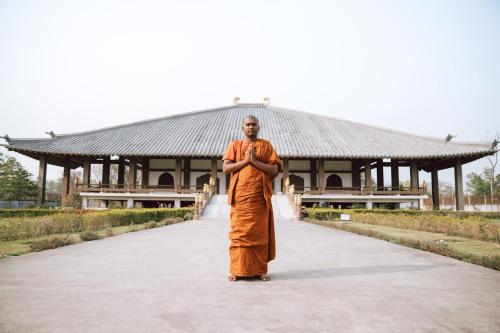 a man in an orange robe standing in front of a building at Hokke Lumbini in Rummindei
