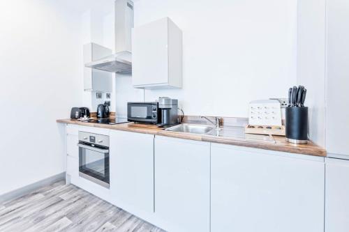 Fantastic 1 Bed Apartment in Wolverhampton في ولفرهامبتون: مطبخ مع دواليب بيضاء ومغسلة