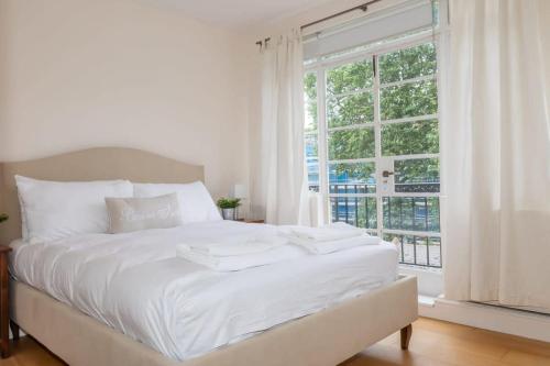 Cama blanca en habitación con ventana grande en Bright & Spacious Top Floor Apartment in Chelsea, en Londres