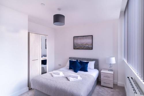 a white bedroom with two beds with blue pillows at Spacious 1 Bed Old Trafford Apartment in Manchester