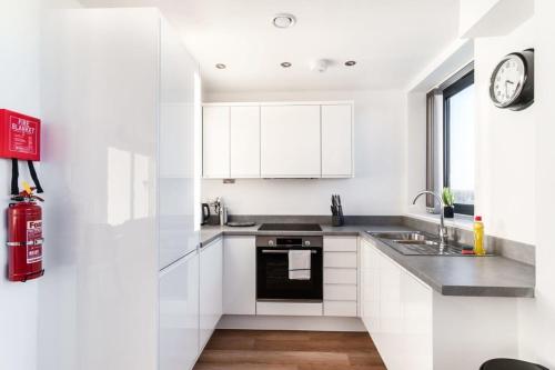 a kitchen with white cabinets and a sink and a clock at StayZeni, Alexandra Rise Manchester 2 Bed Flat in Manchester