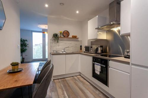 cocina con armarios blancos y mesa de madera en Stunning 2 Bed Flat 5min to Old Trafford Stadium en Mánchester