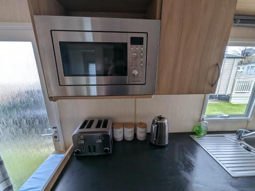 a kitchen with a microwave above a counter top at 3 Bedroom Caravan, Sleeps 8 Lyons Lido Beach in Prestatyn
