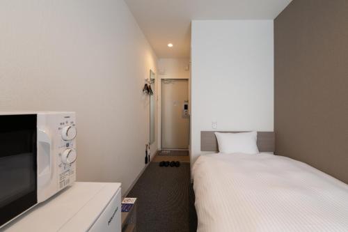 a small room with a bed and a microwave at HOTEL R9 The Yard Sakuragawa in Sakuragawa