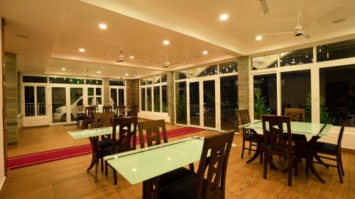 uma sala de jantar com mesas, cadeiras e janelas em Carmel Top Munnar em Munnar