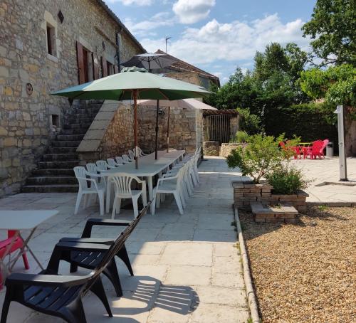 un patio avec tables, chaises et un parasol dans l'établissement Les cigales gîte cigalou, à Grospierres