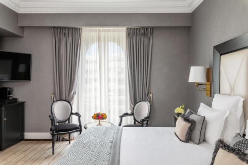 a bedroom with a bed and two chairs and a window at Hôtel Barrière Le Majestic Cannes in Cannes