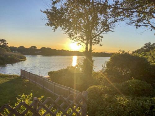 a sunset over a river with a tree and a fence at Waterfront Fun Dogs Welcome in Dennis
