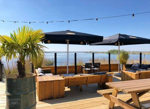 a patio with tables and umbrellas on a beach at Luxe en ruim chalet met airco bij Leekstermeer in Matsloot