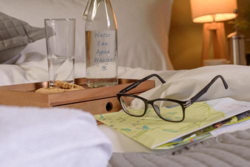 a pair of glasses sitting on a bed with a bottle at The Downe Arms Hotel in Castleton