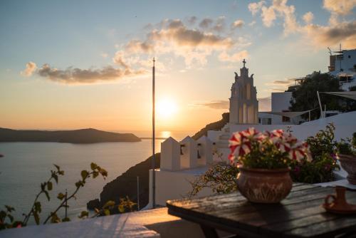 a sunset over the ocean with a church on a cliff at Lithies Traditional Homes in Firostefani