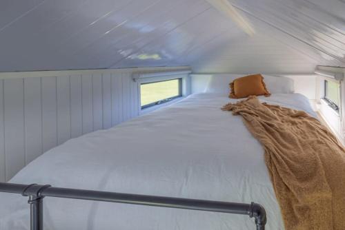 ein weißes Bett in einem kleinen Zimmer mit Fenster in der Unterkunft Blackiron Tiny House 