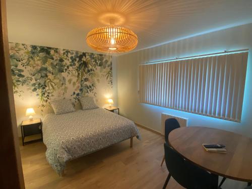 1 dormitorio con cama, mesa y lámpara de araña en Chez Isa, en Failly